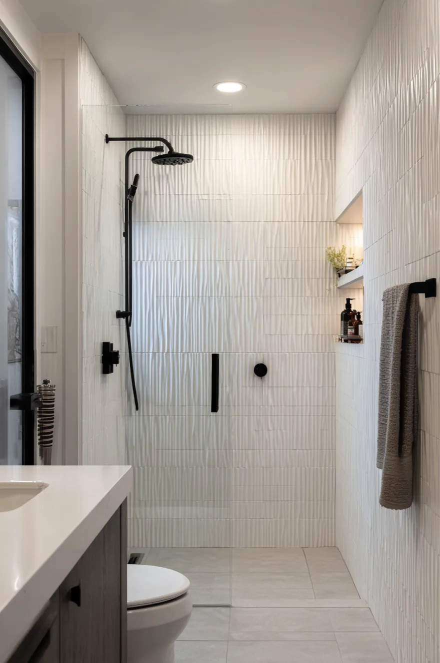 A modern bathroom shower featuring heavily textured 3D white fluted tiles on the walls, contrasting matte black shower fixtures, a built-in niche, and a sleek glass door.