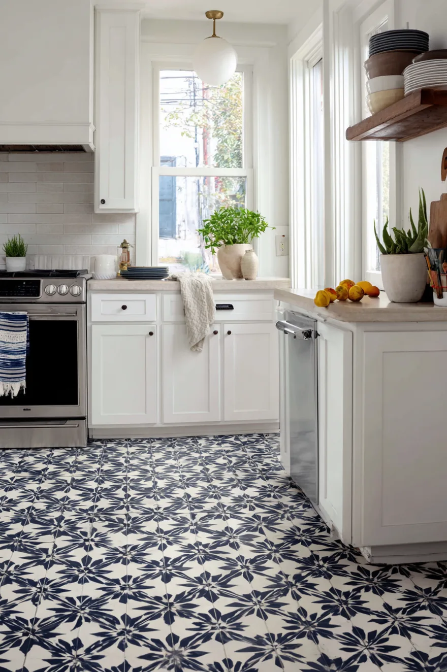 Geometric tile kitchen floor in deep navy and white star-and-cross encaustic cement pattern with flat white shaker cabinets and honed stone countertops in natural daylight.